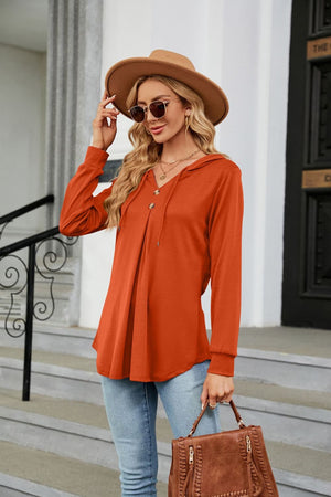Orange hooded henley top with button detail and pleats.