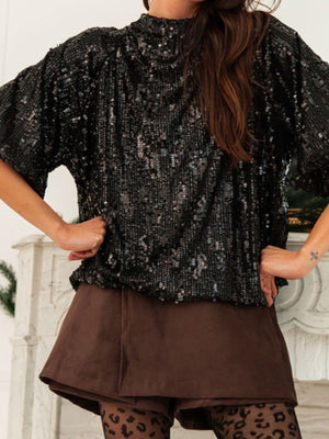 Black sequin tie-back blouse with mock neck and short sleeves, styled with brown shorts.