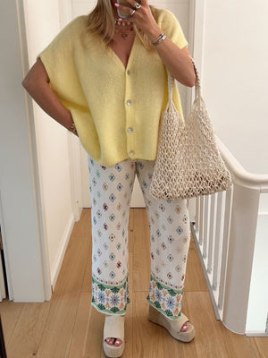 Pastel yellow cap sleeve mohair cardigan with pearl buttons, worn open over printed pants.