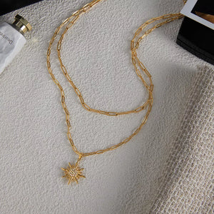 Layered gold necklace with radiant sun pendant featuring crystal accents.