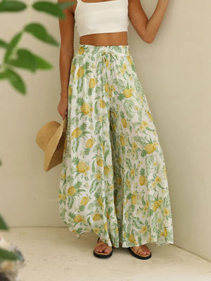 Pineapple print palazzo trousers in white with yellow and green tropical pattern, featuring a drawstring waist and wide legs.