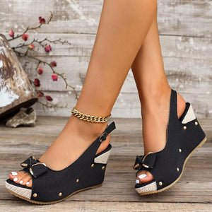 Black peep toe wedge sandals with decorative bow and adjustable strap.