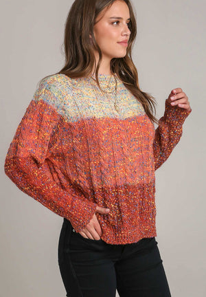 Ombre cable knit crewneck sweater in orange-red with flecks of color.