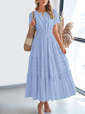 Light blue V-neck tiered maxi dress with smocked waist and short sleeves, styled with a straw bag.