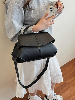 Black textured geometric flap shoulder bag with contrast stitching and adjustable strap.