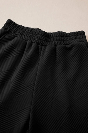 Black quilted knit lounge pants with smocked waistband and geometric pattern detail.