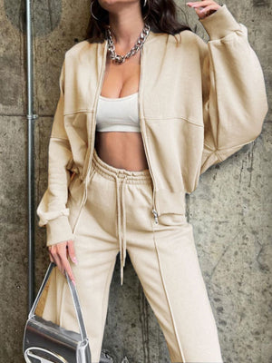 Tan zip-up jacket and drawstring pants set with white crop top and silver bag.