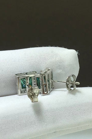 Green emerald cut stud earrings with diamond accents on a white cloth.
