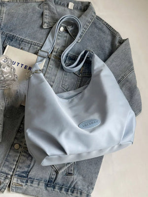 Light blue canvas shoulder bag with adjustable strap and oval patch detail.