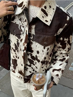 Buttoned collared cow print jacket with chest pockets and button front closure.