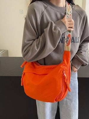 Orange woven strap small crossbody bag with braided zipper pulls and a patterned strap.