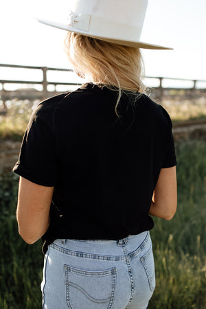 Black graphic t-shirt with cuffed short sleeves worn by a woman in light wash jeans.