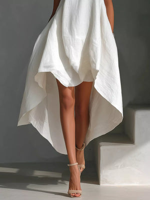 White asymmetrical sleeveless flowing dress with a high-low hem and beige strappy heels.