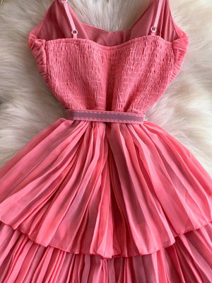 Pink belted midi dress with spaghetti straps and pleated skirt.