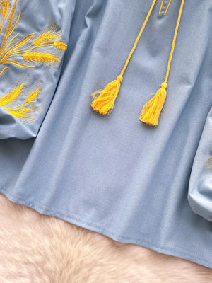 Blue tie-neck blouse with yellow wheat embroidery and tassels.