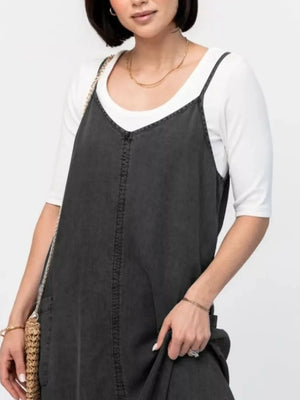 Gray purple denim maxi dress with V-neck and adjustable straps, worn over a white top.
