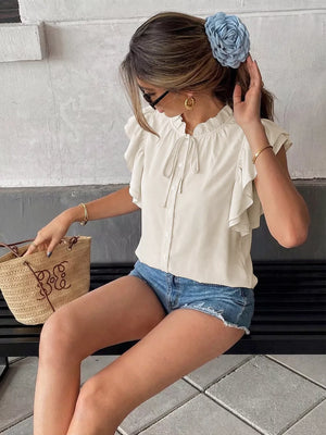 Beige tie-neck shirt with ruffle sleeves and button front, styled casually.