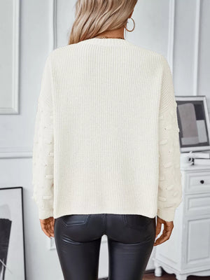 Chic ivory knit sweater with textured sleeve details and pockets, styled with black pants.