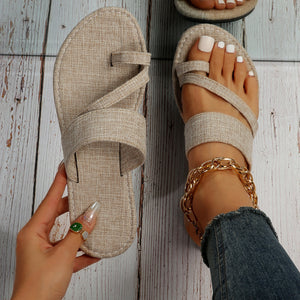 Beige crisscross toe loop sandals with fabric straps and a gold chain anklet.