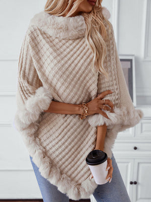Beige knit poncho with faux fur trim and diamond pattern, styled with jeans and jewelry.
