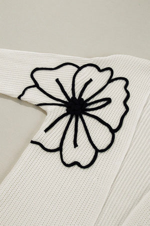Ivory acrylic knit cardigan with black floral appliqué detail on sleeve