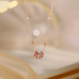 Rose gold necklace with bezel-set clear crystals and a cluster of colorful rings.