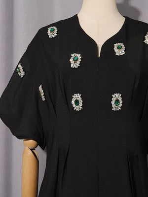 Black midi dress with puff sleeves and rhinestone-embellished green jewels.