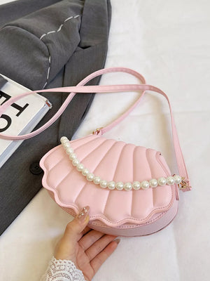 Pink shell crossbody bag with pearl embellishment and a long strap.