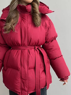 Burgundy puffer trench coat with hood and belted waist, shown on a woman.