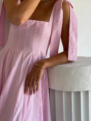 Pink bow-tie shoulder maxi dress with square neckline and pleated skirt detail.