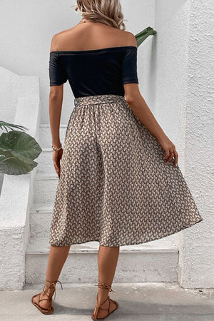 Black off-shoulder midi dress with a patterned A-line skirt and tie-up sandals.