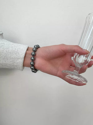 Dark gray beaded bracelet with clasp on wrist, holding a glass.