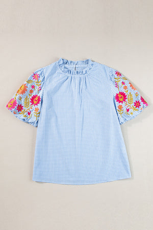 Light blue gingham blouse with embroidered floral sleeves and ruffled neckline.