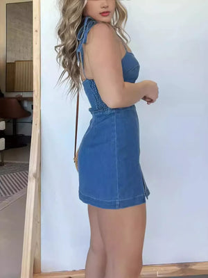 Blue denim mini dress with tie straps, smocked waist, and side slit hem.