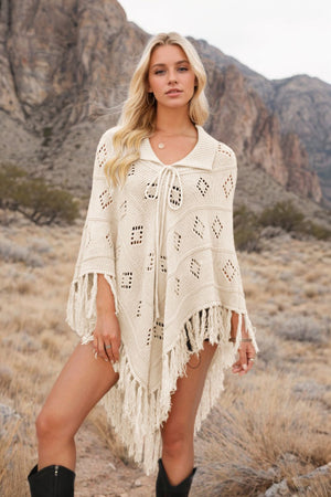 Cream knit poncho with geometric pattern and fringe, tie neck, collared.