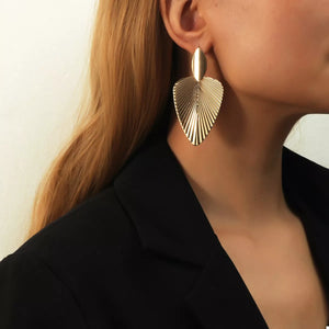 Gold leaf silhouette dangle earrings with textured detail.