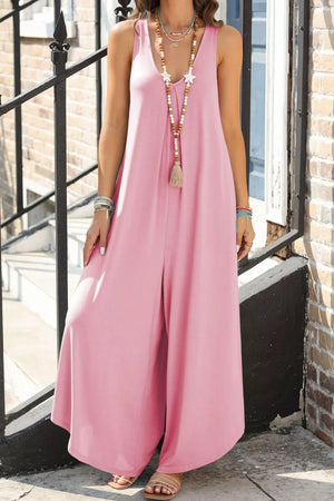 Pink wide leg jumpsuit with V-neck and tassel necklace.