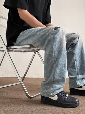 Men's light wash distressed wide-leg jeans with paisley pattern and ripped knees.