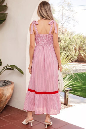Maxi dress with pink and white stripes, smocked bodice, bow knot straps, and red trim.