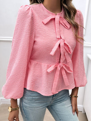 Pink textured peplum blouse with bow details and puff sleeves.