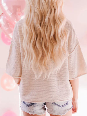 Beige knit sweater with textured pattern and short sleeves, styled with denim shorts.
