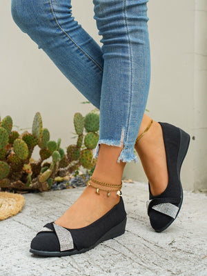 Black slip-on wedge flats with rhinestone bow detail.