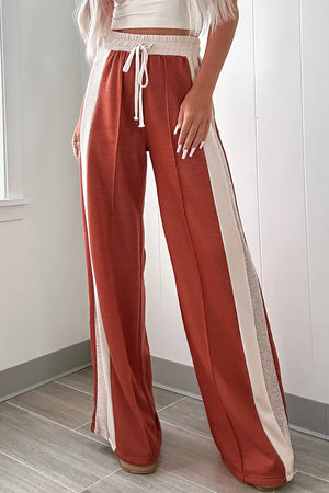 Terracotta-red track pants with contrast cream side panels and drawstring waist.