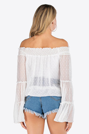 White dotted swiss off-shoulder blouse with ruffle bell sleeves and smocked neckline.