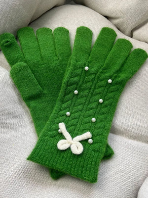 Green cable knit gloves with pearl embellishments and a white bow detail.