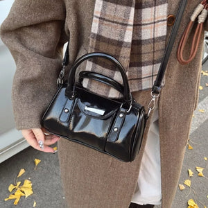 Black patent barrel crossbody bag with top handles and silver hardware