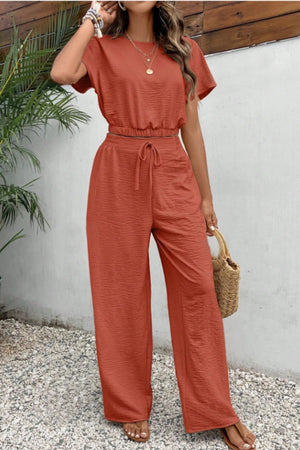 Rust textured crop top and wide-leg trousers with drawstring waist, styled with a straw bag.