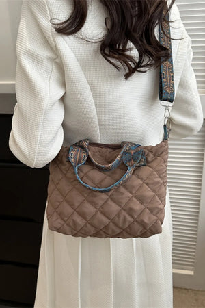 Quilted satchel bag in taupe with a patterned strap and handles.