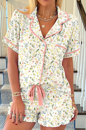 Ivory pajama set with pink trim, featuring a floral print, button-up top, and ruffled shorts with a bow.