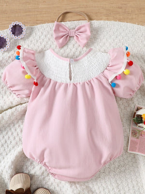 Blush pink cotton baby romper with smocked white yoke and pom-pom trim. Includes matching bow headband.